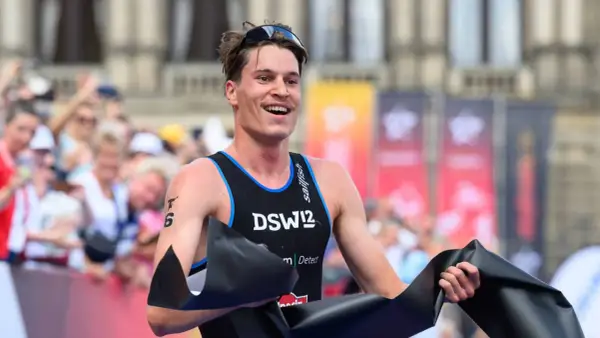 Lächelnder Athlet durchbricht die Ziellinie beim Triathlon Sprint, jubelnd mit schwarzem Band.